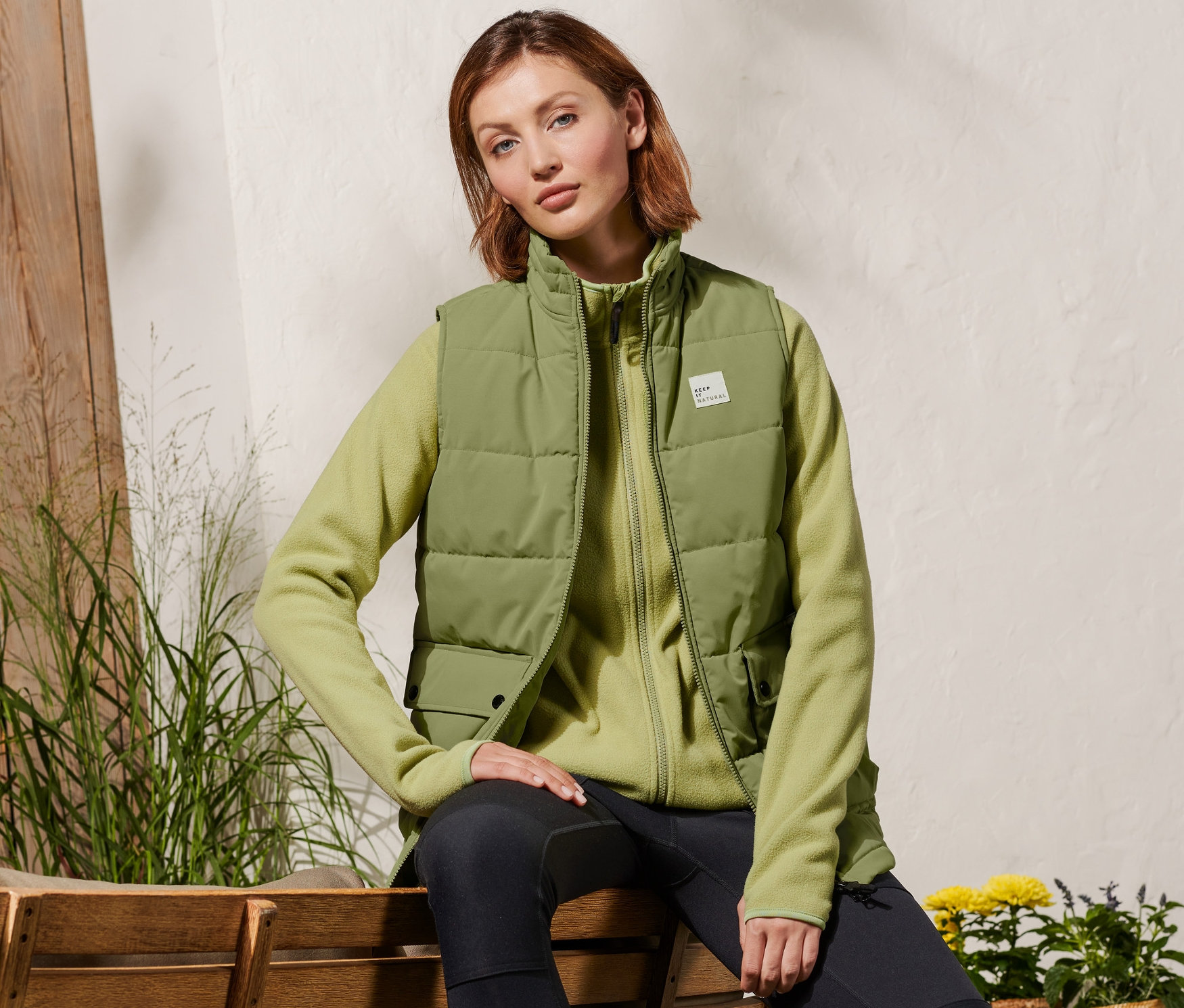 Kobieta siedzi na ławce i ma na sobie kamizelkę pikowaną.