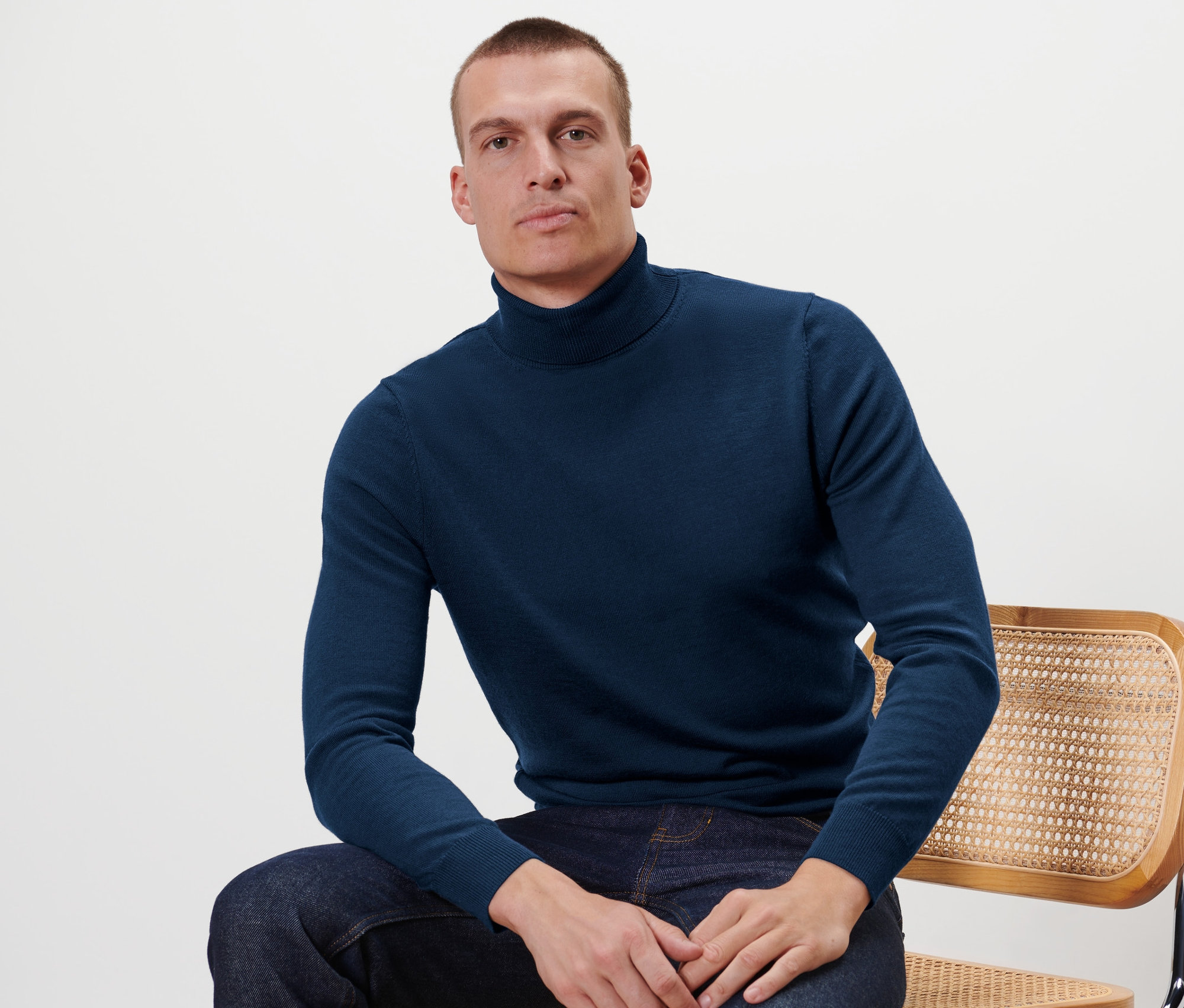 Mężczyzna siedzi na krześle i ma na sobie granatowy sweter z wełny merino.
