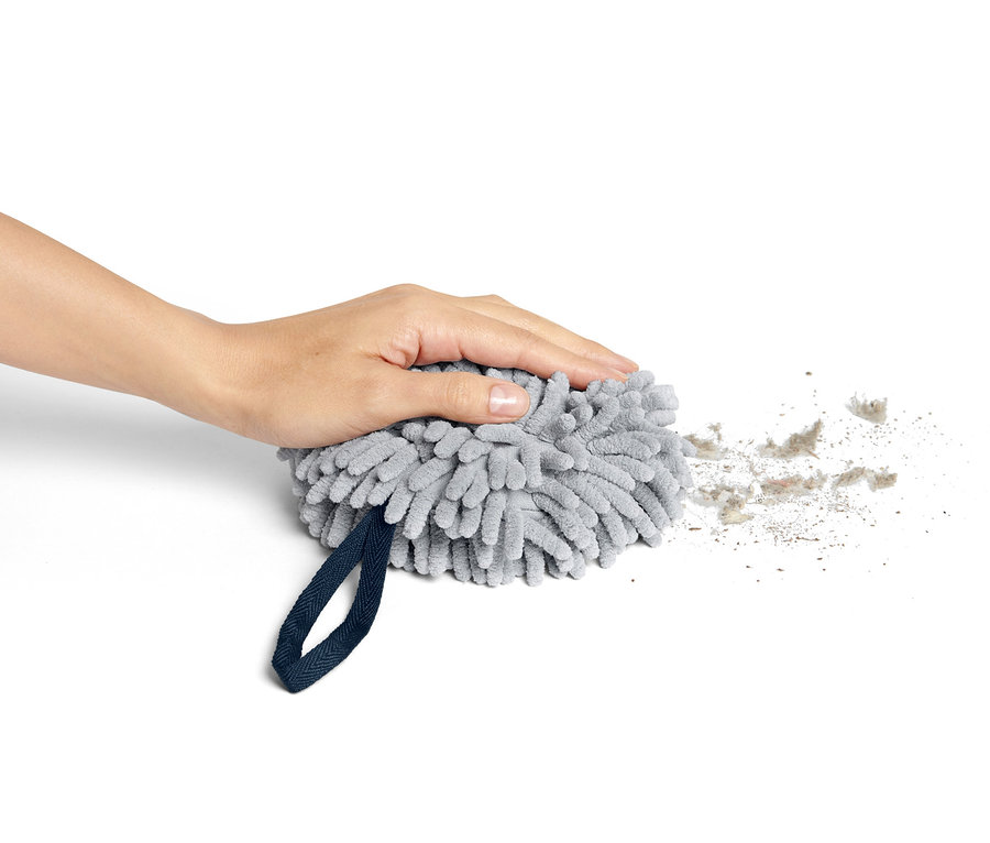 Ręka naciska na szarą kulę-ścierkę osuszającą, wokół której znajduje się kurz.