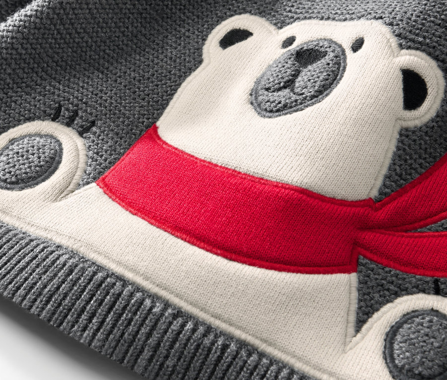 Zbliżenie na sweter dziecięcy z aplikacją przedstawiającą misia polarnego w czerwonym szaliku.