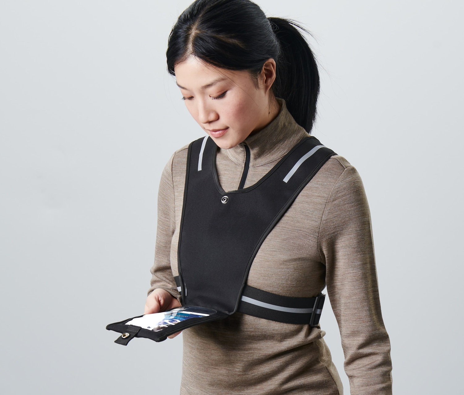 Kobieta trzyma smartfon w kieszeni czarnej kamizelki do biegania.