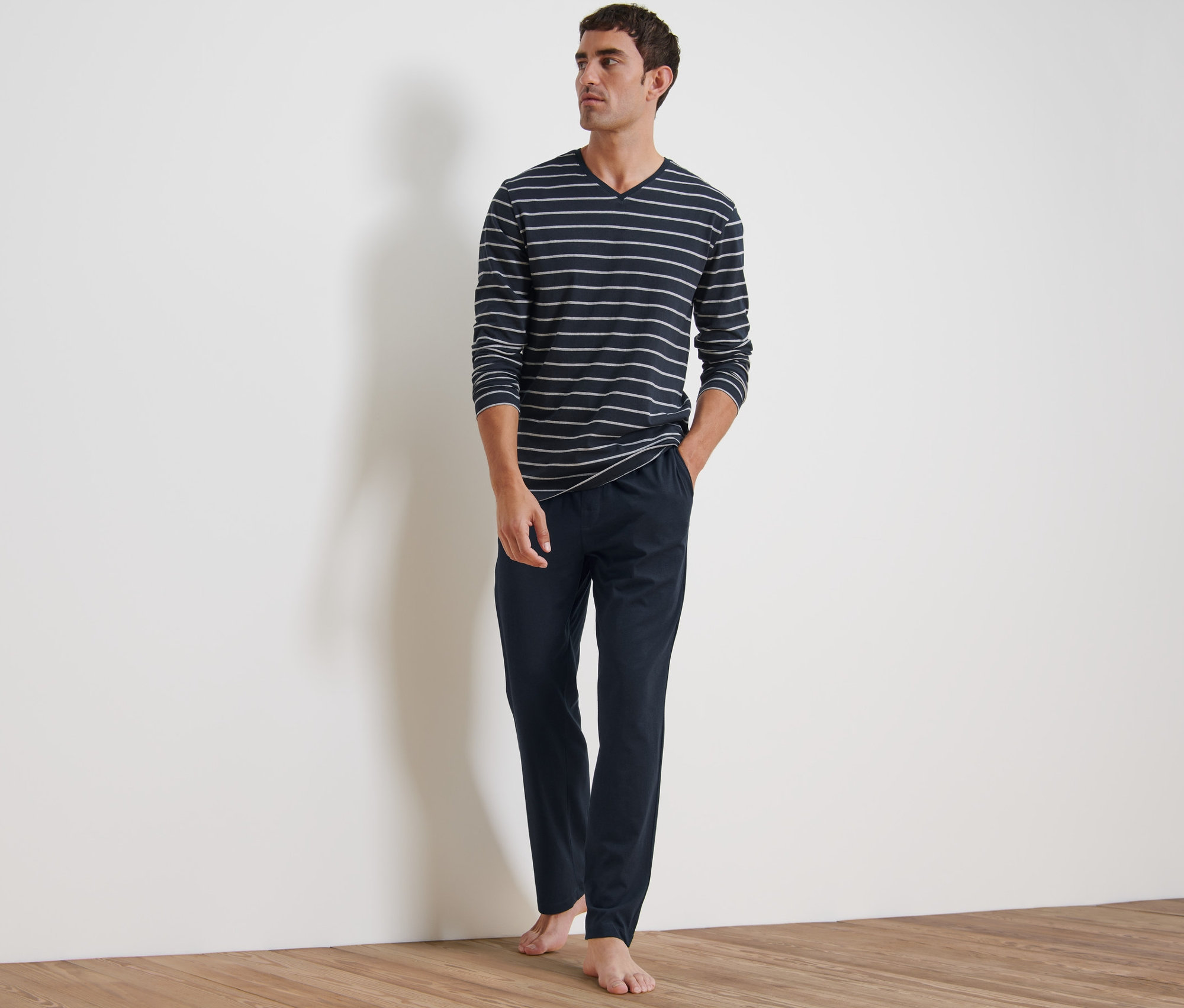 Mężczyzna stoi i ma na sobie piżamę. Składa się z bluzki z długim rękawem w paski i granatowych spodni.
