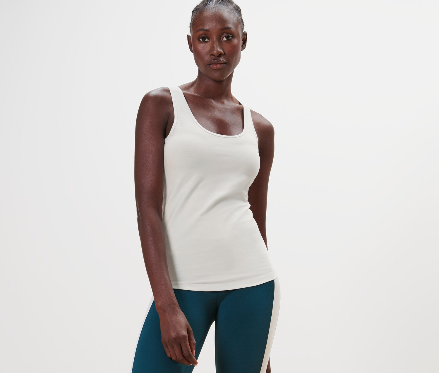 Stojąca ciemnoskóra kobieta ma na sobie kremowy top i zielone legginsy.