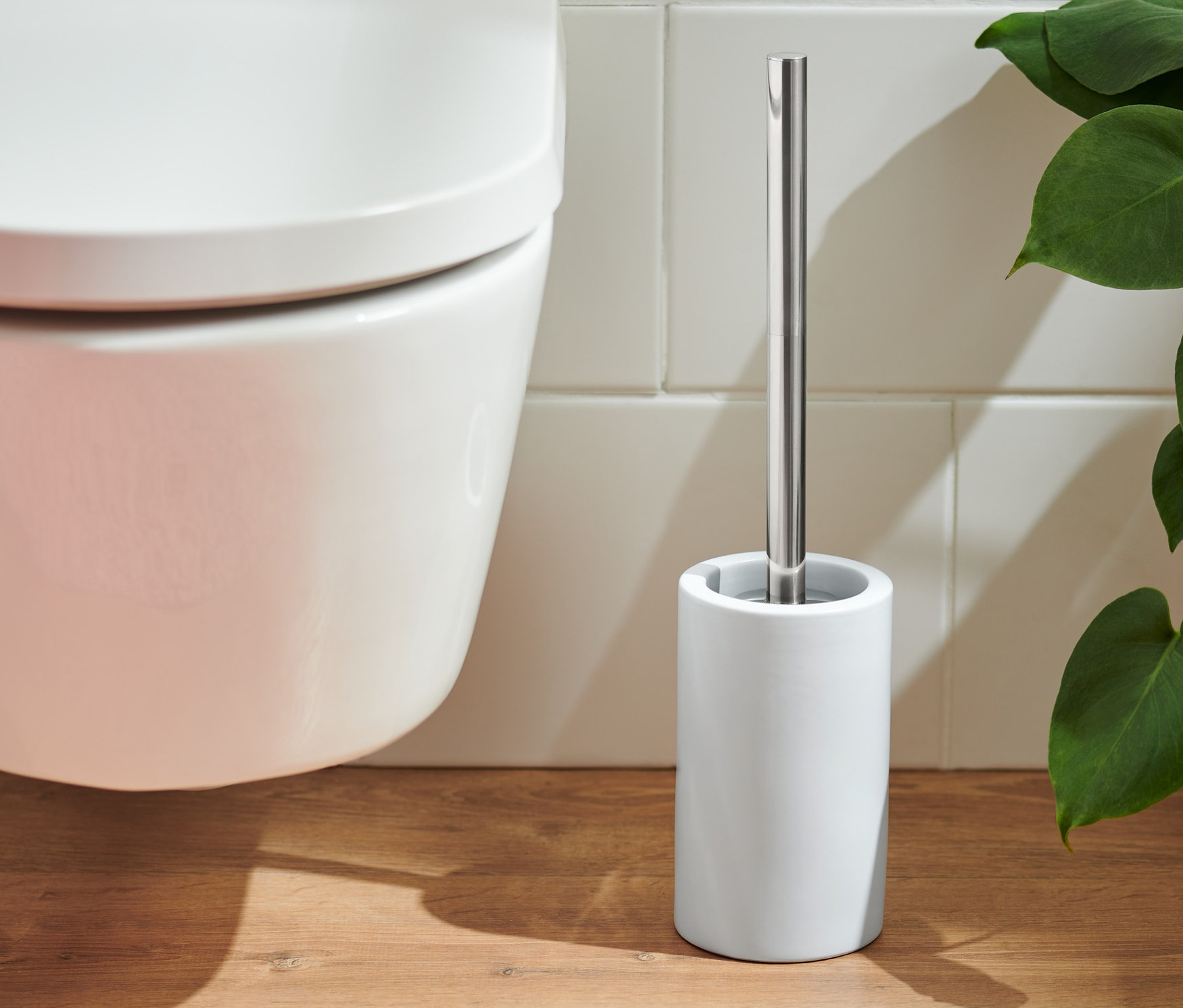 Toaleta i biała szczotka do WC stoją na drewnianej podłodze obok różowego dywanu.