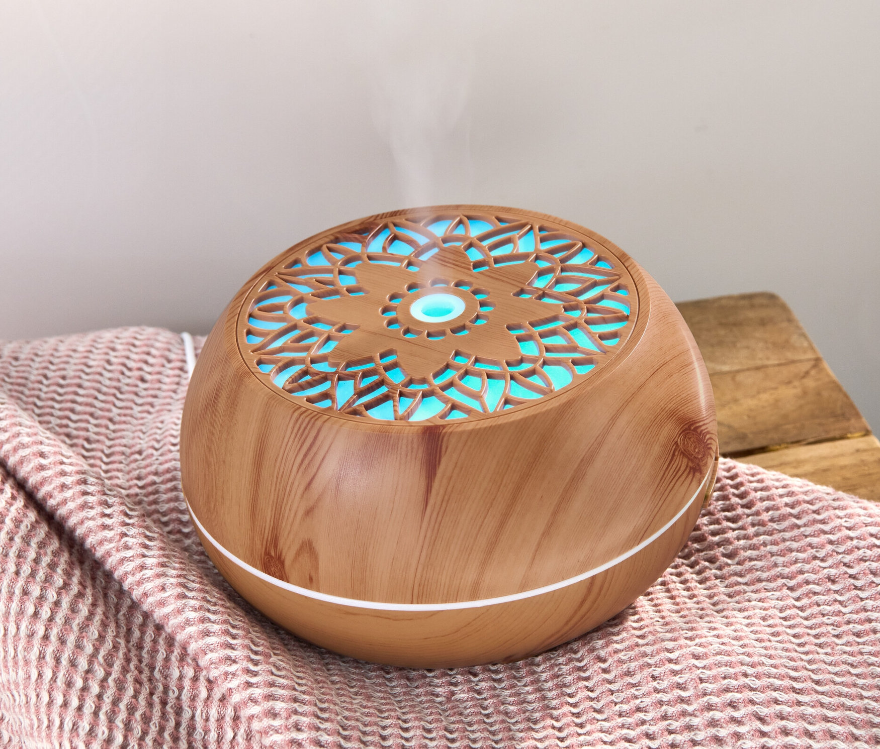 Dyfuzor zapachów z głośnikiem Bluetooth® stoi na różowym kocu, z którego unosi się para.