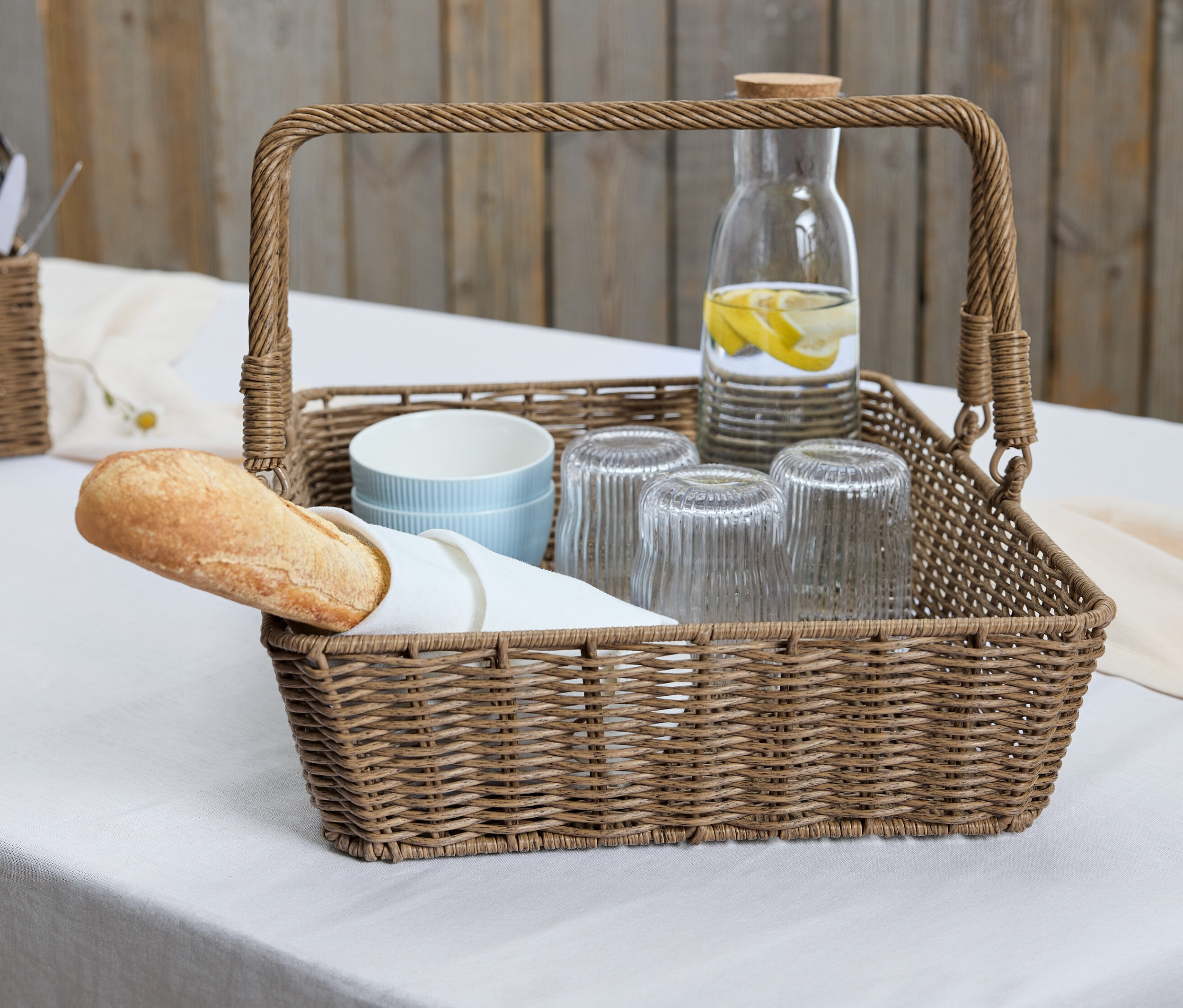 Koszyk z tacą zawiera bagietkę, szklanki i karafkę z cytryną.