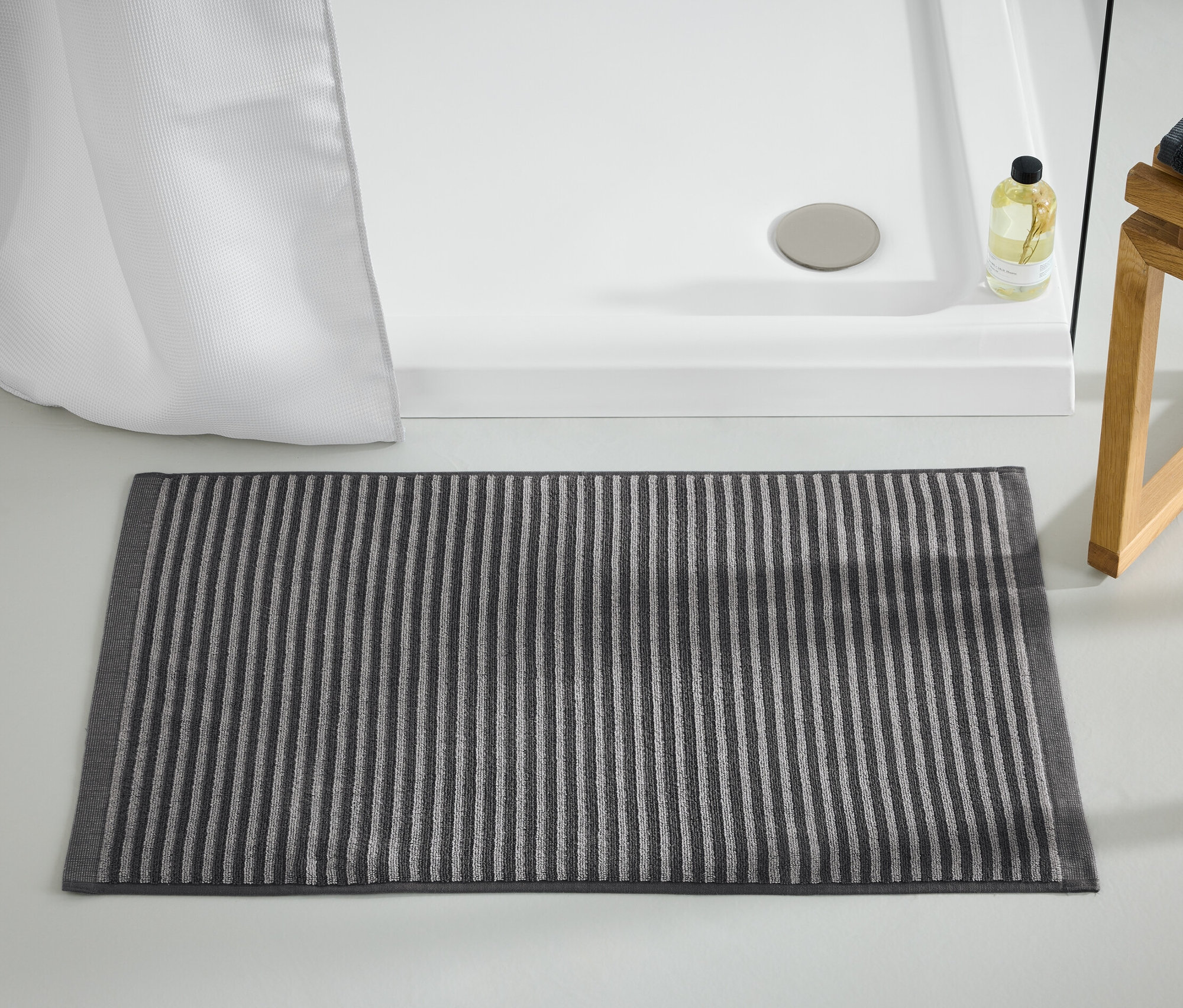Antracytowy dywanik łazienkowy leży na podłodze obok kabiny prysznicowej.
