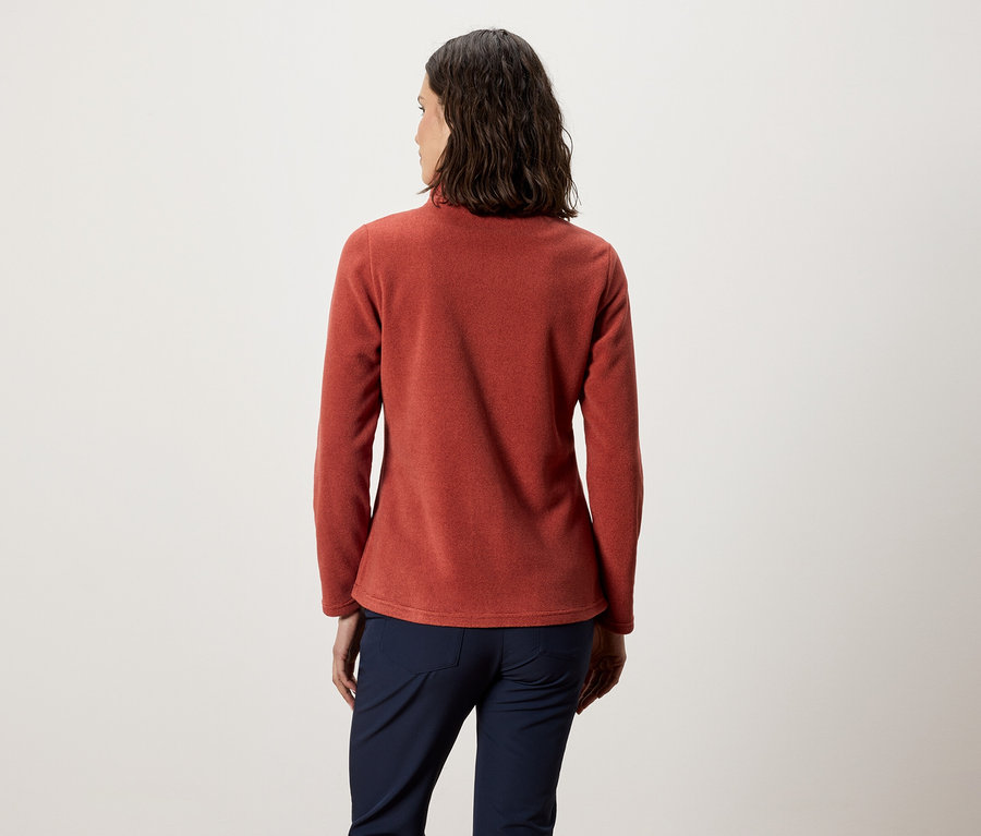 Kobieta tyłem do kamery ma na sobie pomarańczową bluzę polarową i granatowe spodnie.