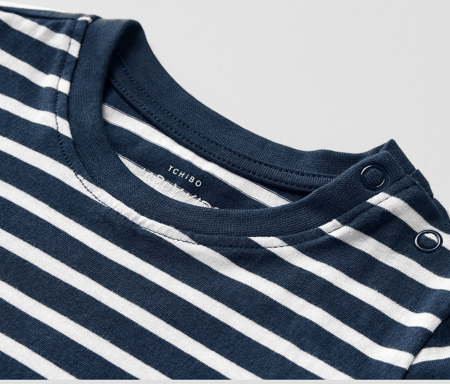 Zbliżenie na dziecięcą koszulkę z długim rękawem w niebiesko-białe paski, zapinaną na guziki na ramieniu.