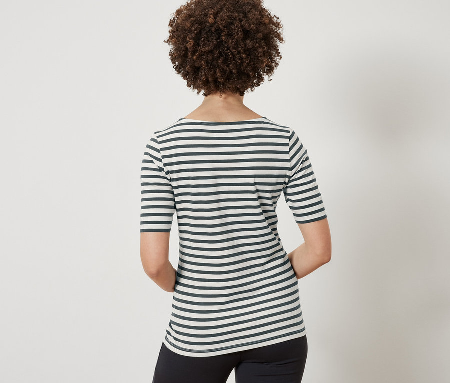 Widok z tyłu kobiety z brązowymi kręconymi włosami, ubranej w koszulkę z półdługim rękawem w zielone paski i czarne spodnie.