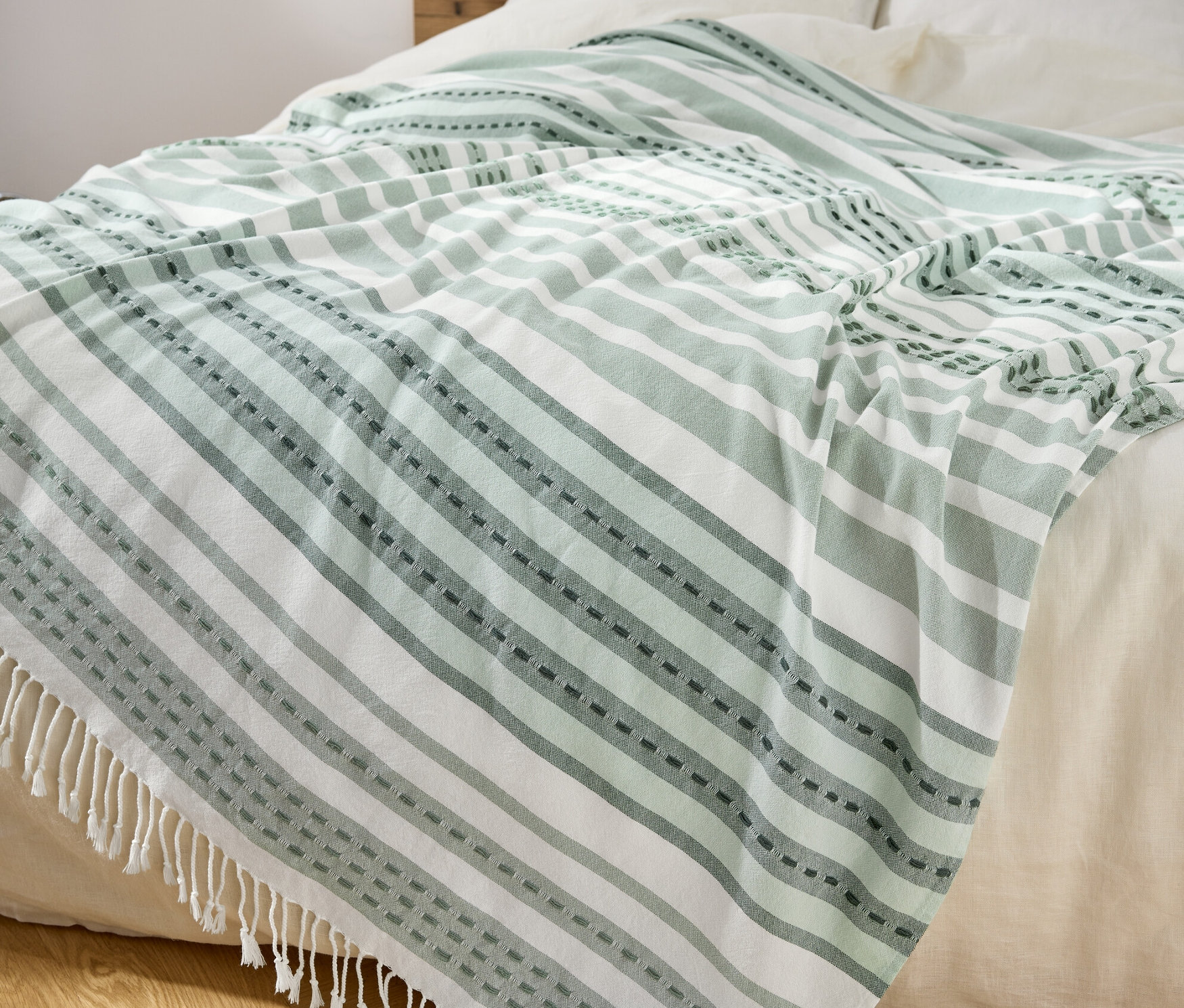 Na łóżku leży pled w zielono-białe paski z frędzlami.