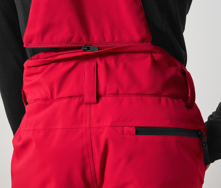 Szczegół czerwonych spodni na szelkach z czarnym zamkiem błyskawicznym.