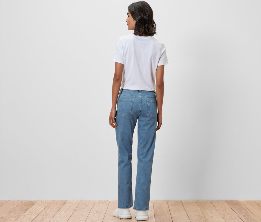 Kobieta stoi tyłem do aparatu, ubrana w dżinsy o kroju „Kira” i biały T-shirt.