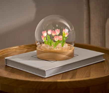 LED-DIY-Bastel-Set z tulipanami w szklanej kopule na książce na okrągłym stoliku.