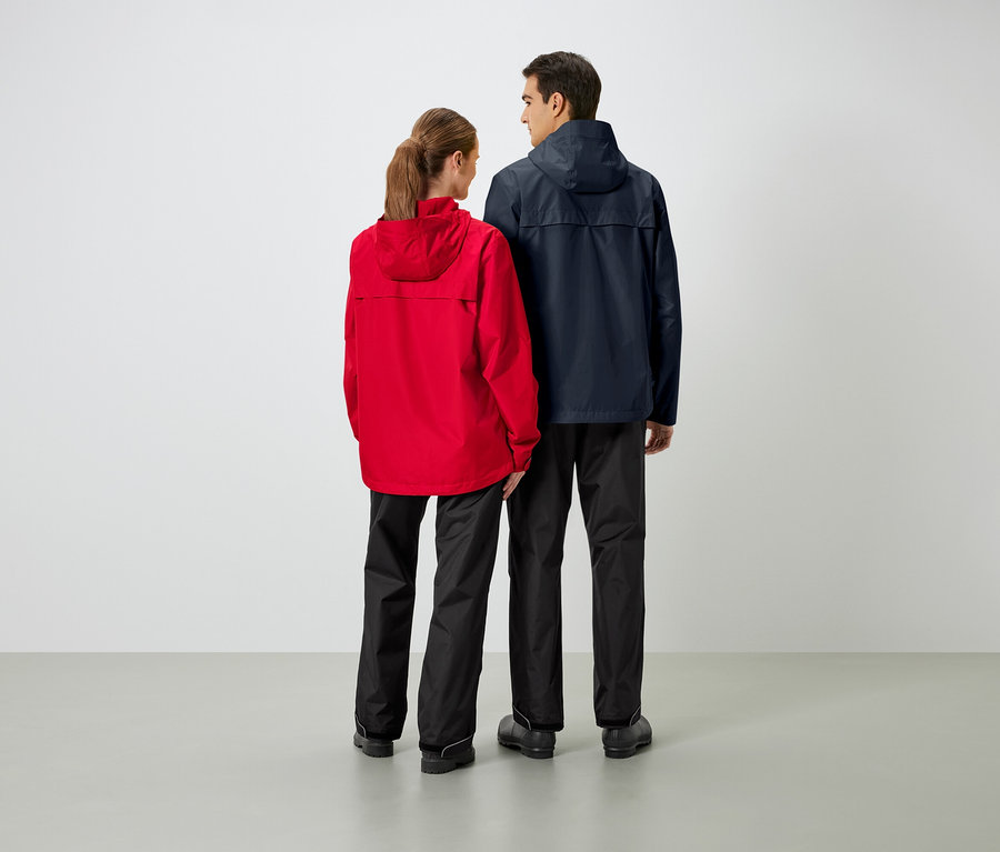 Dwie osoby stoją tyłem do kamery, ubrane w kurtki przeciwdeszczowe i spodnie przeciwdeszczowe.