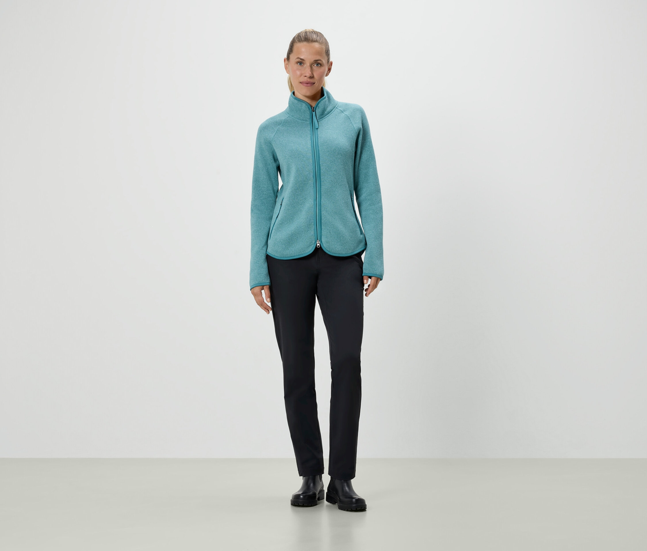 Kobieta stoi w turkusowej kurtce polarowej i czarnych spodniach.