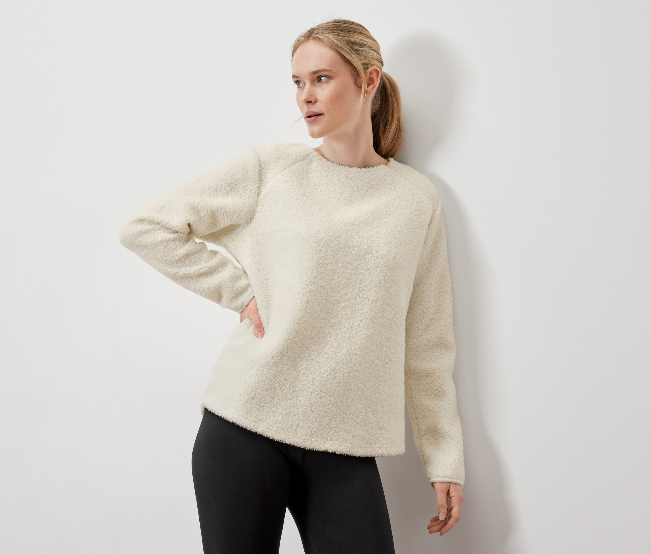 Kobieta pozuje w kremowym swetrze i czarnych legginsach.