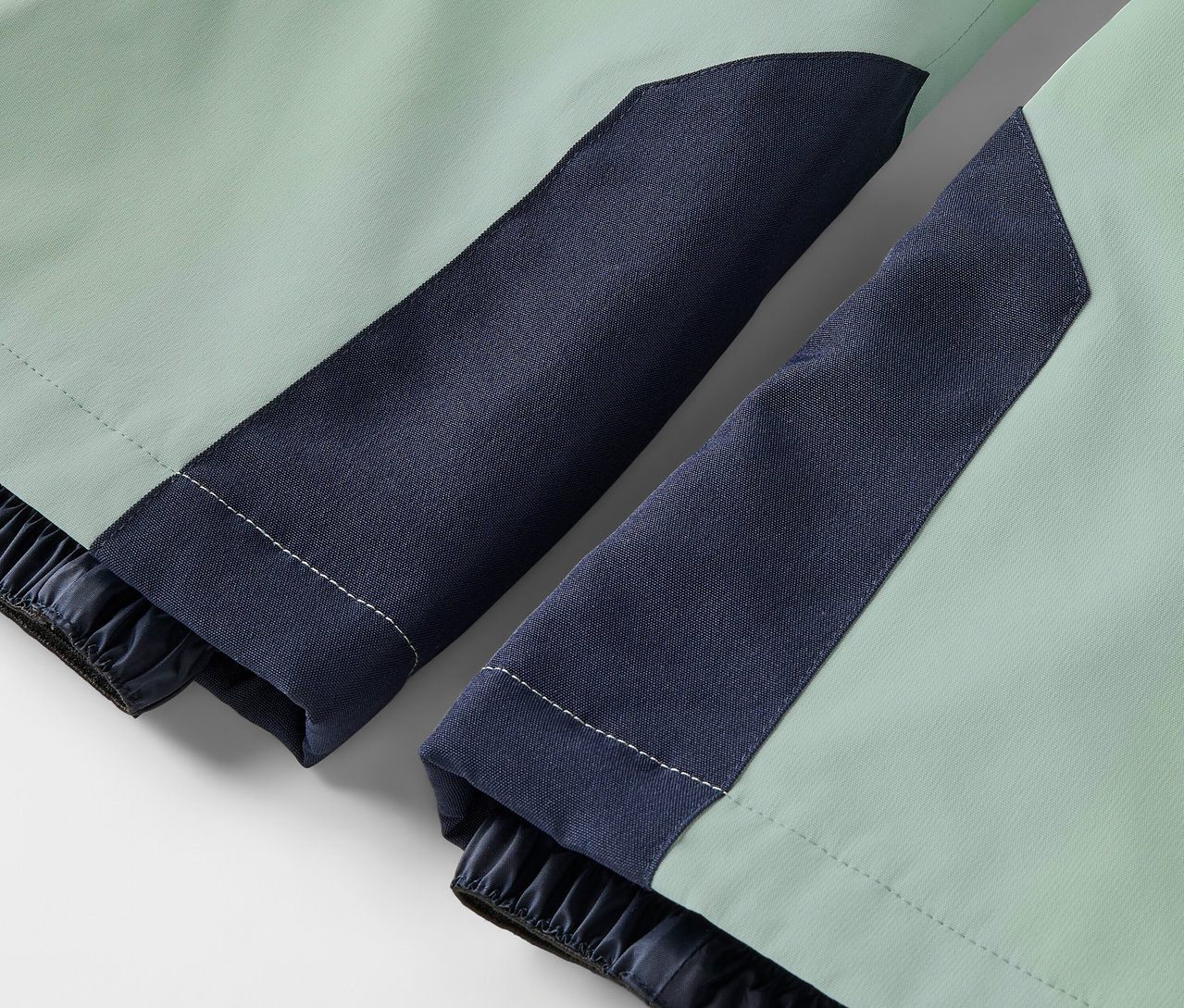 Zbliżenie jasnozielonej kurtki z granatowymi rękawami i elastycznymi mankietami.