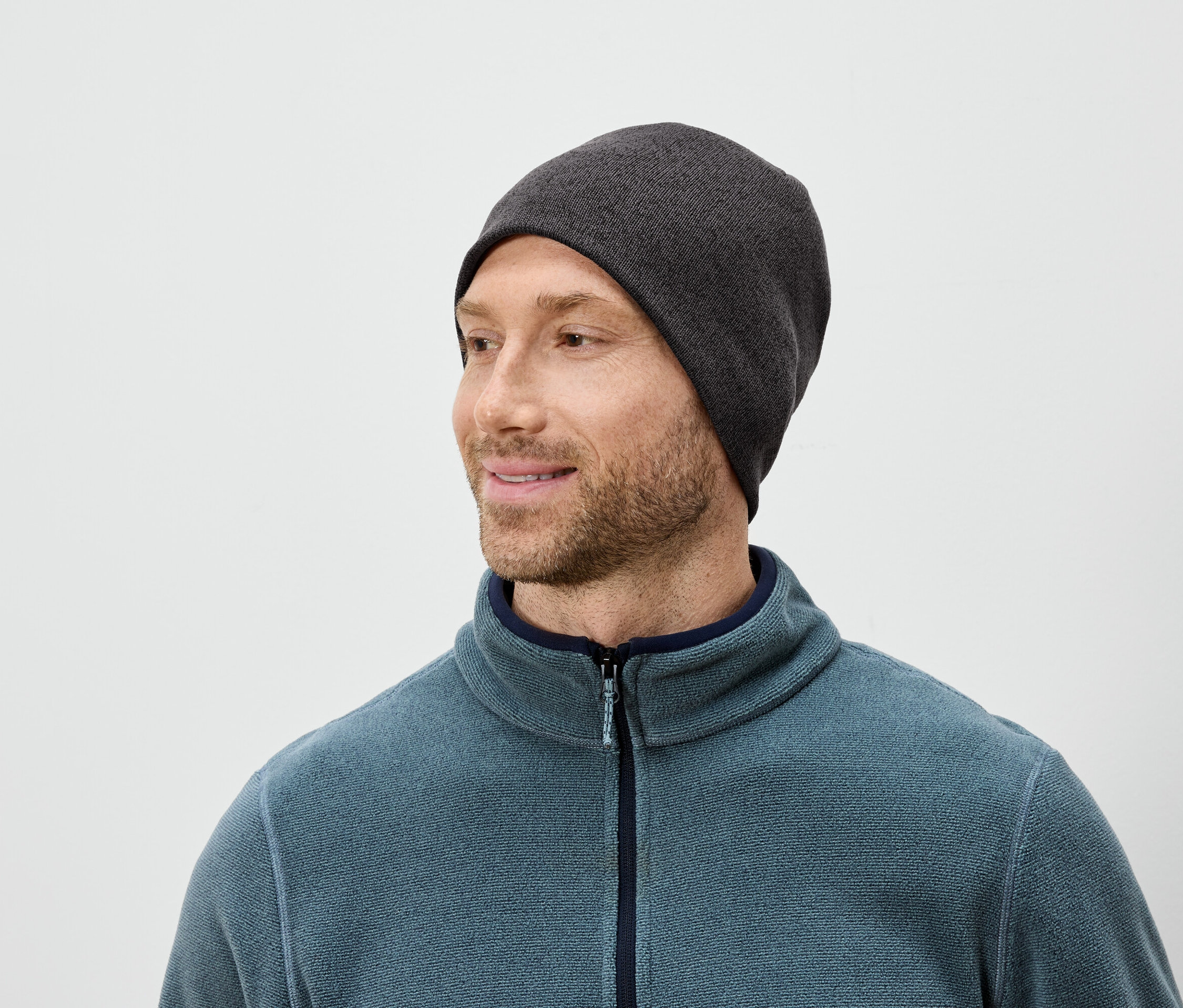 Mężczyzna z brodą w szarej czapce i niebieskim polarze patrzy w prawo.