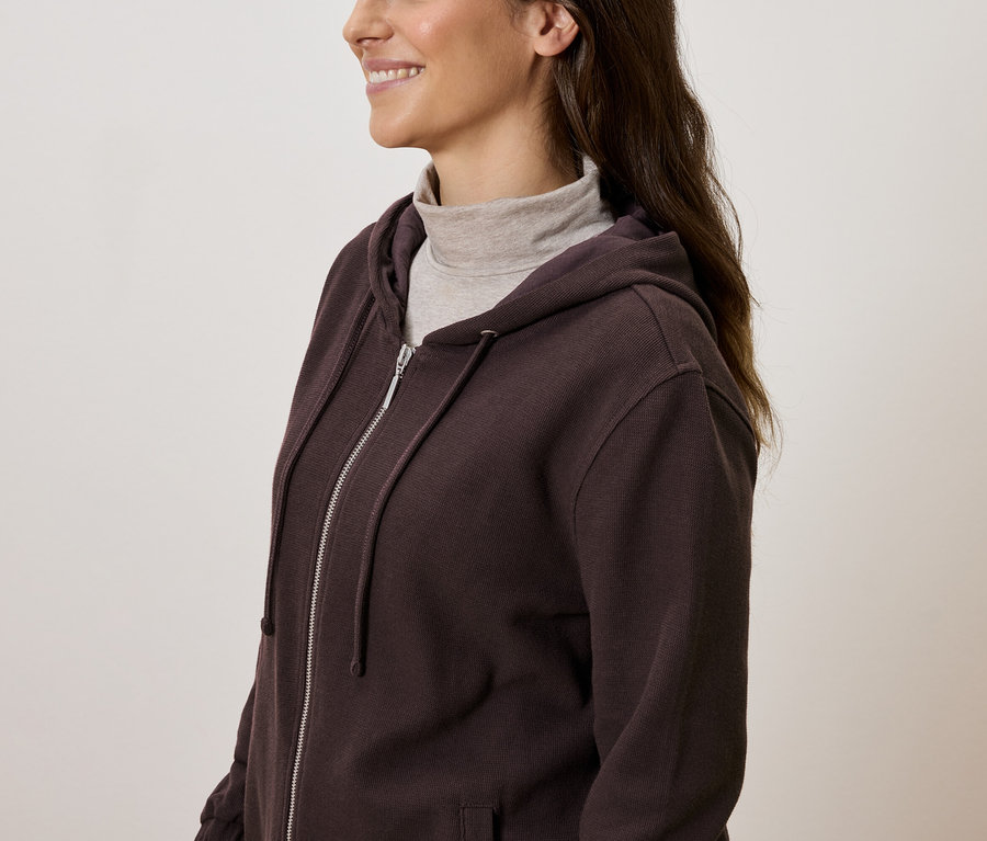 Kobieta w brązowej bluzie z kapturem zapinanej na zamek i golfem.