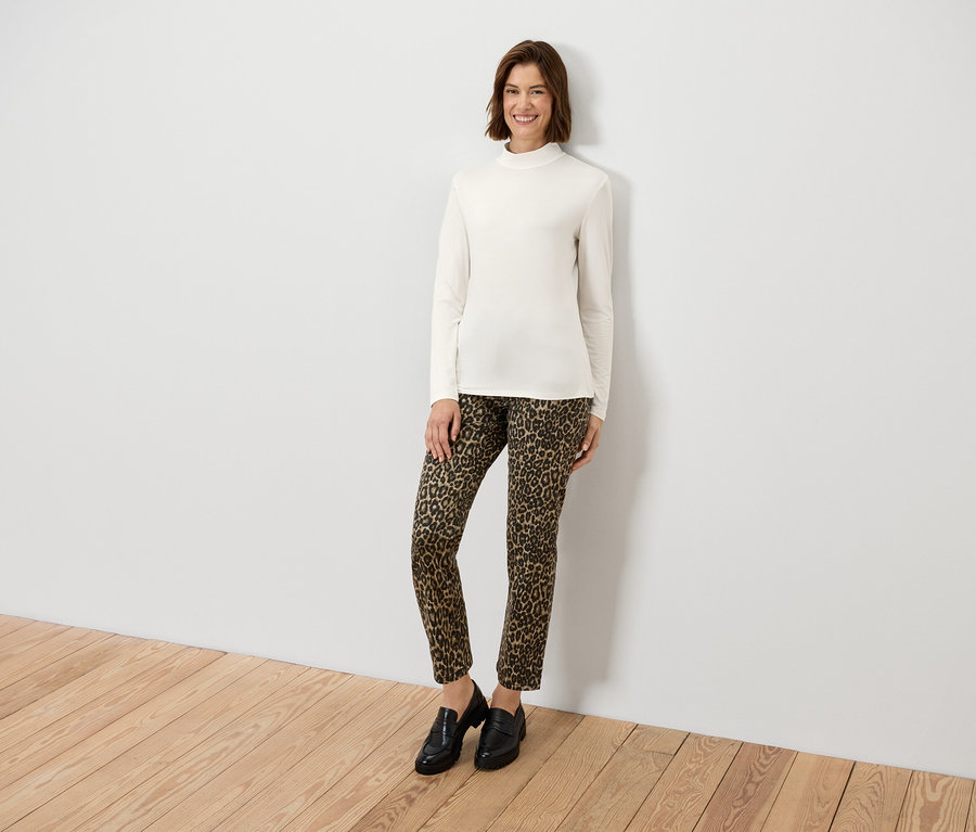 Kobieta pozuje w kremowej bluzce z długim rękawem i spodniach w zwierzęcy wzór.