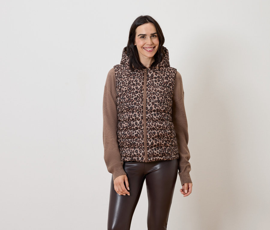 Kobieta pozuje w brązowej kamizelce z kapturem w zwierzęcy wzór i brązowych skórzanych spodniach.