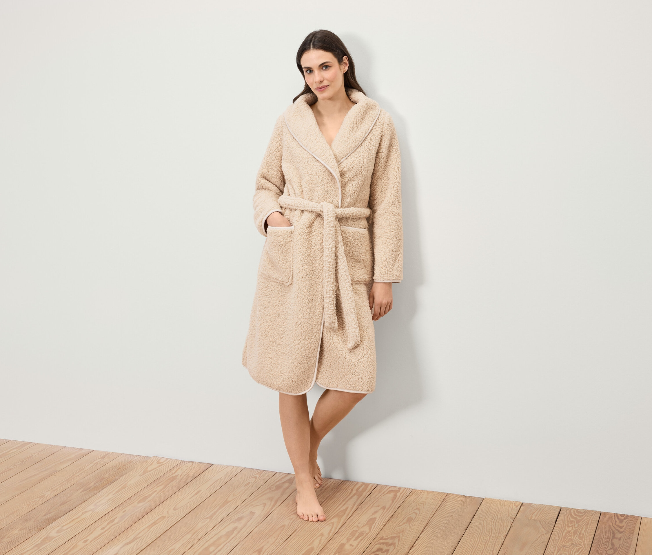 Kobieta stoi i ma na sobie puszysty szlafrok z paskiem.
