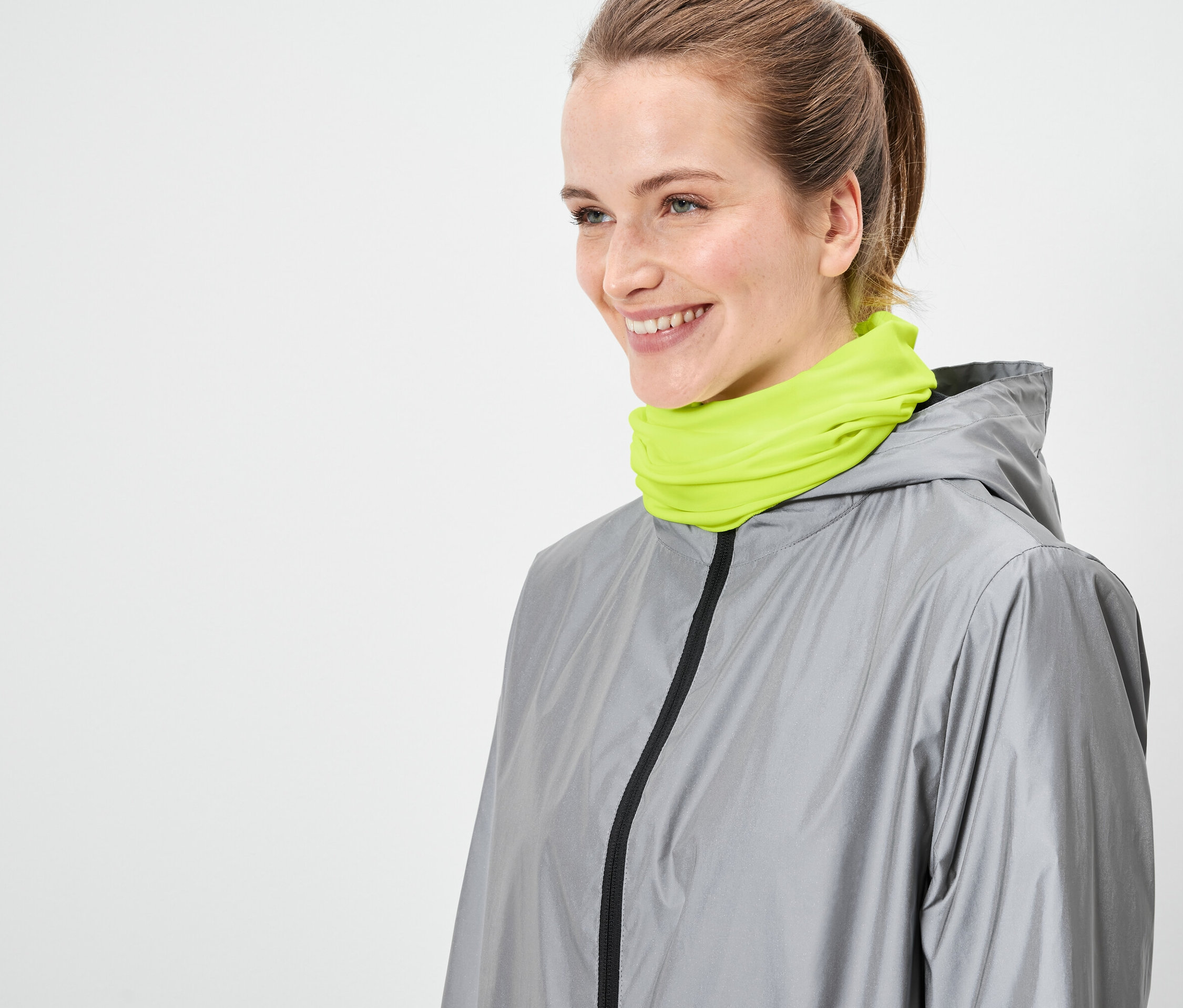 Kobieta ma na sobie szarą kurtkę i neonowo zielony szal.