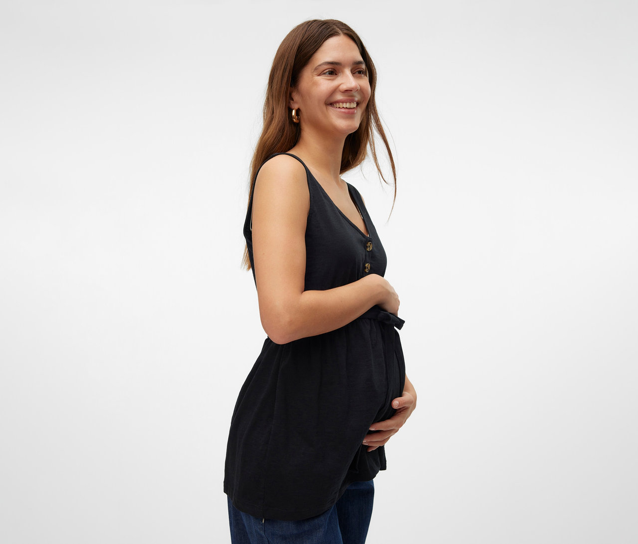 Uśmiechnięta kobieta trzyma się za brzuch, ubrana w czarny top do karmienia piersią MAMALICIOUS „MLEVI LIA” i dżinsy.