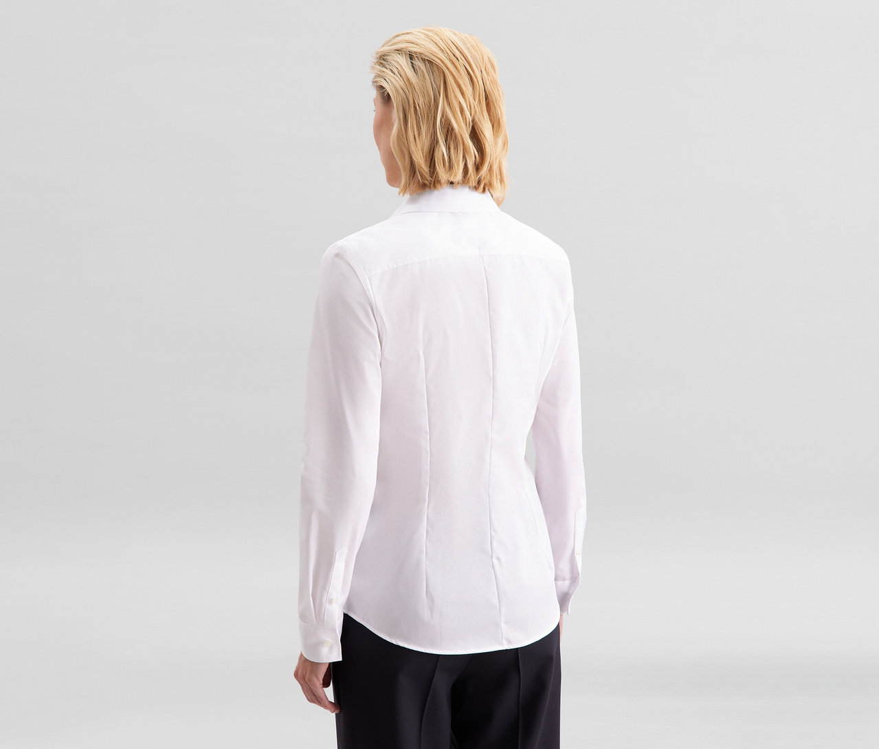 Kobieta od tyłu, ubrana w białą bluzkę Seidensticker Slim Fit non iron i czarne spodnie.