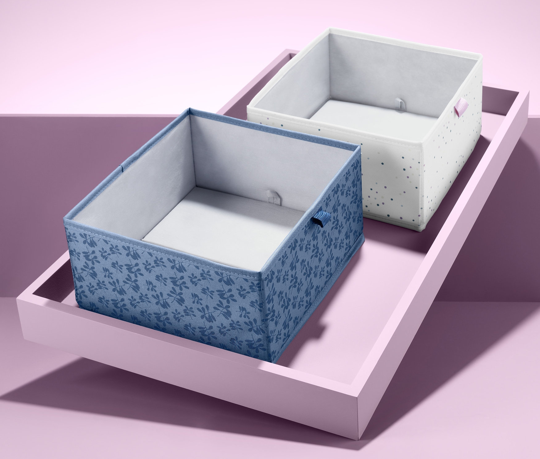 Dwa kwadratowe organizery do szuflad na różowej tacy.
