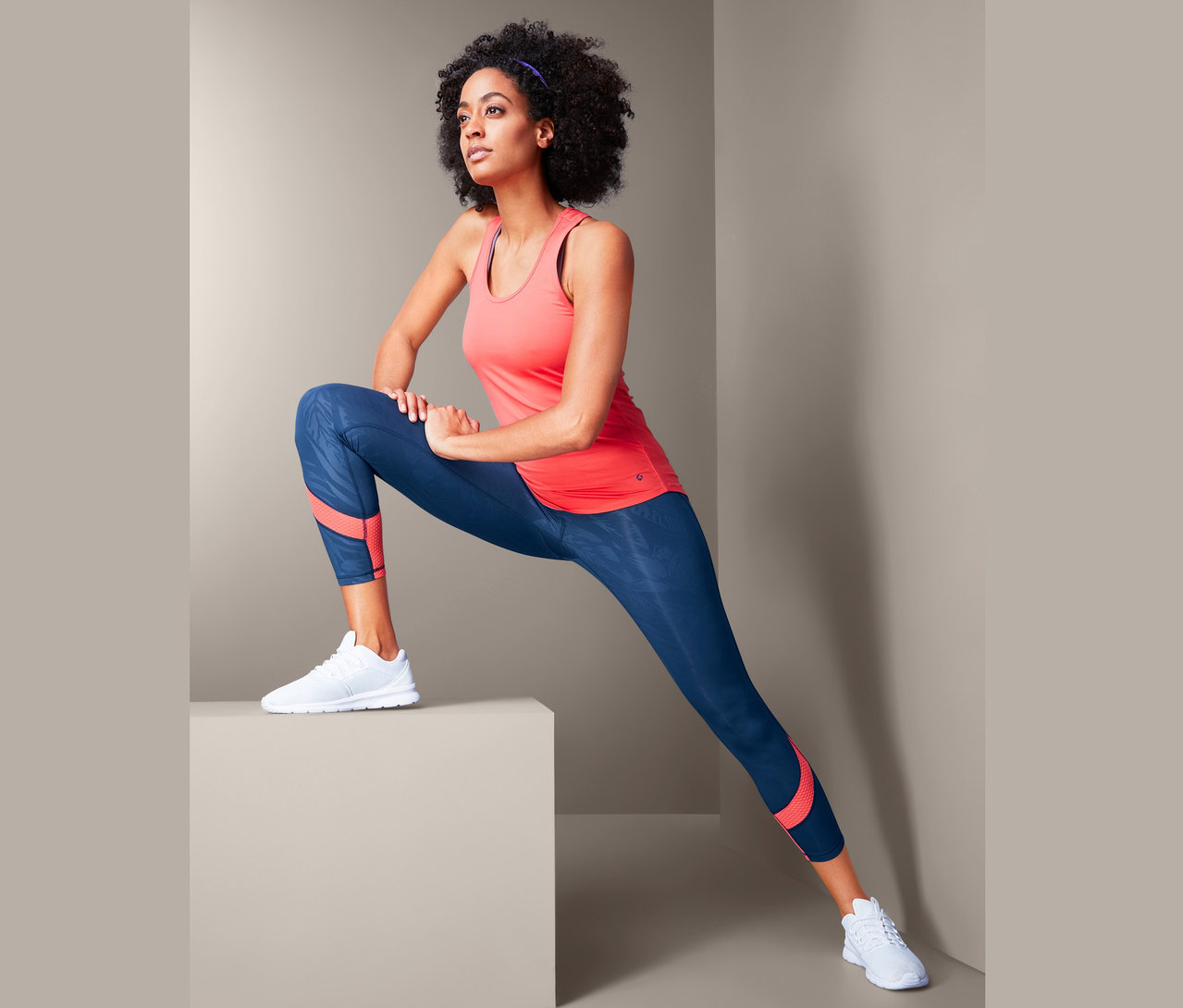Kobieta rozciąga się w damskich legginsach sportowych o długości 7/8, granatowych z koralowymi wstawkami.