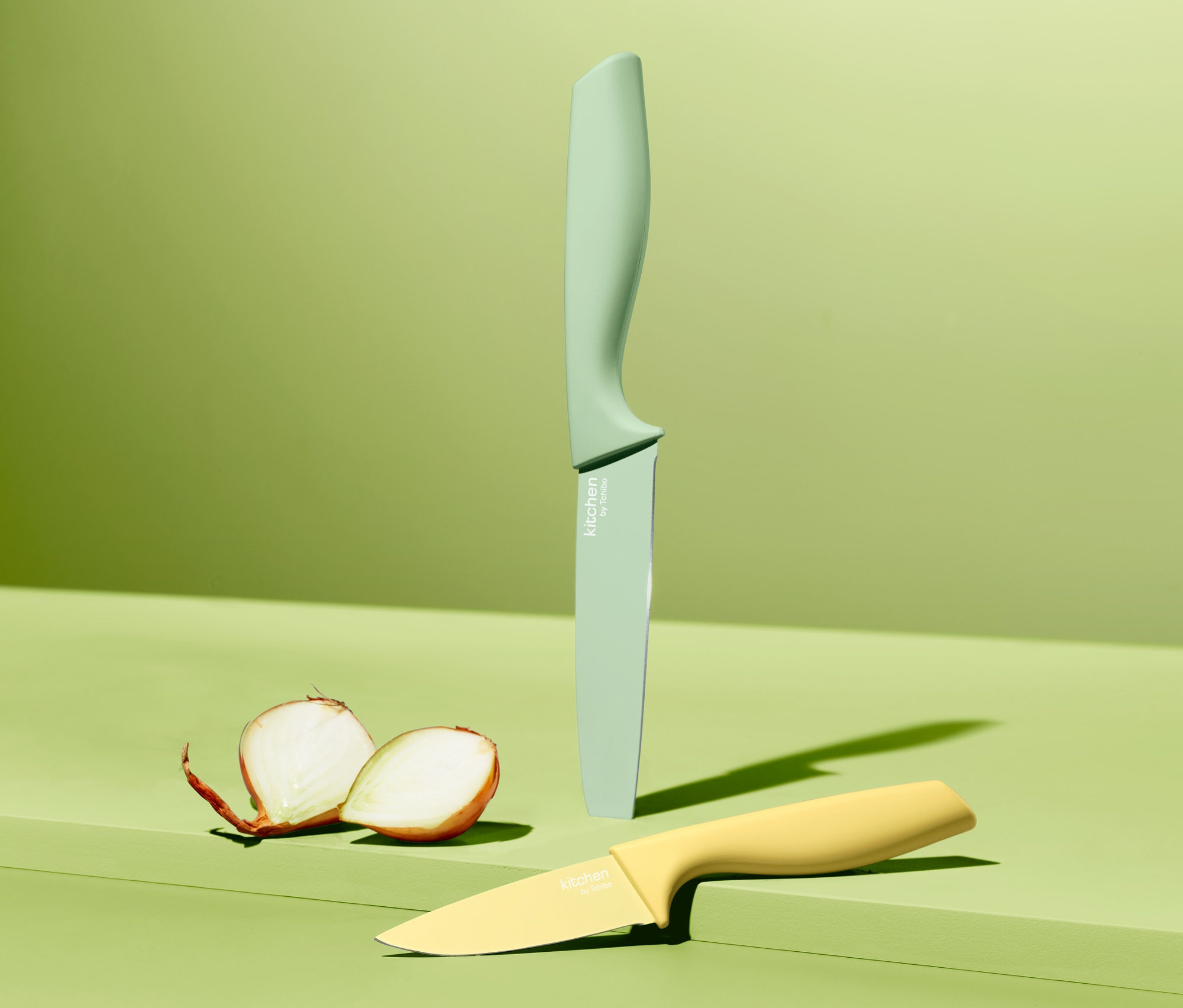 Dwa noże kuchenne z kompletu noży kuchennych (2 sztuki) i przekrojona cebula na zielonym tle.
