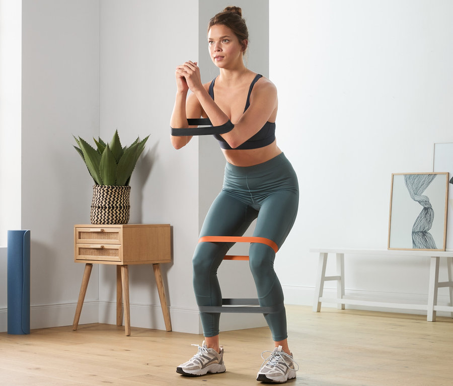 Kobieta robi przysiady z 3 taśmami treningowymi.