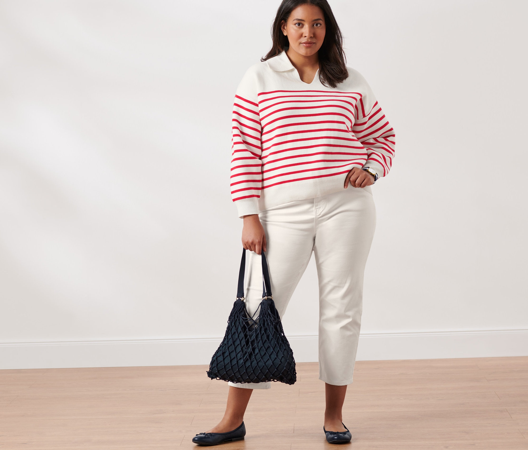 Kobieta pozuje w biało-czerwonym swetrze z dzianiny z kołnierzem, spodniach dżinsowych o kroju slimfit, balerinach skórzanych, z torbą i zegarkiem kwarcowym ze stali nierdzewnej.