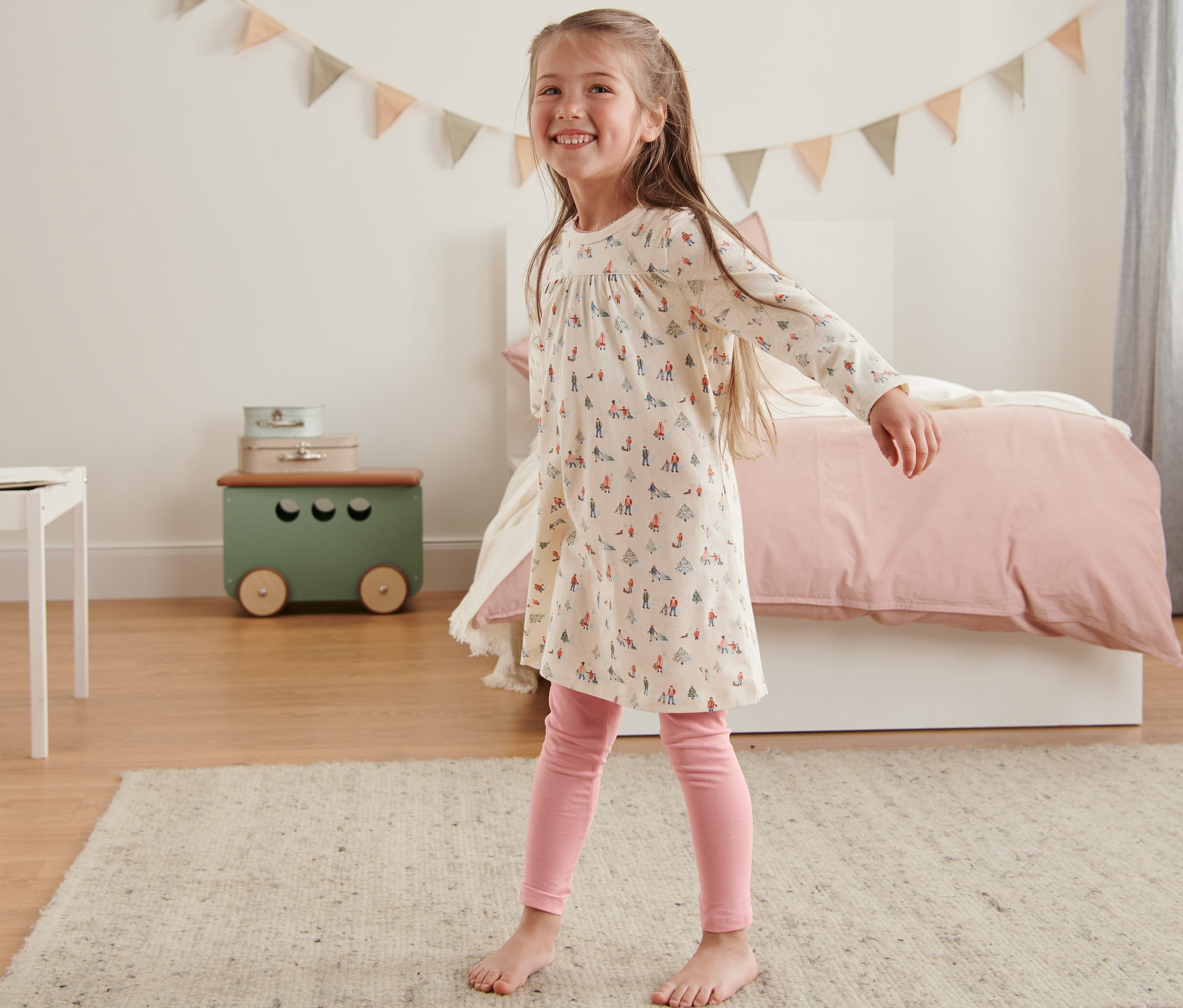 Uśmiechnięta dziewczynka tańczy w dziecięcej koszuli nocnej z legginsami w sypialni.