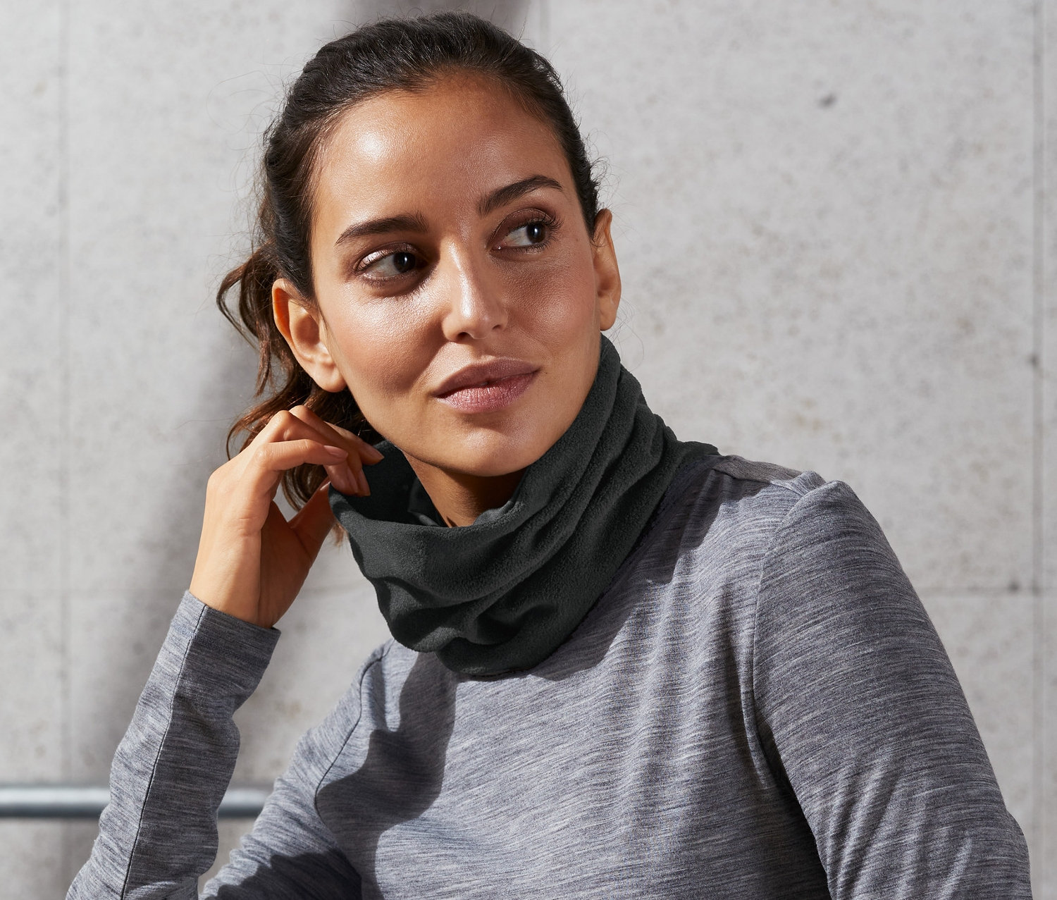 Kobieta siedzi i ma na sobie chustę wielofunkcyjną na szyi.