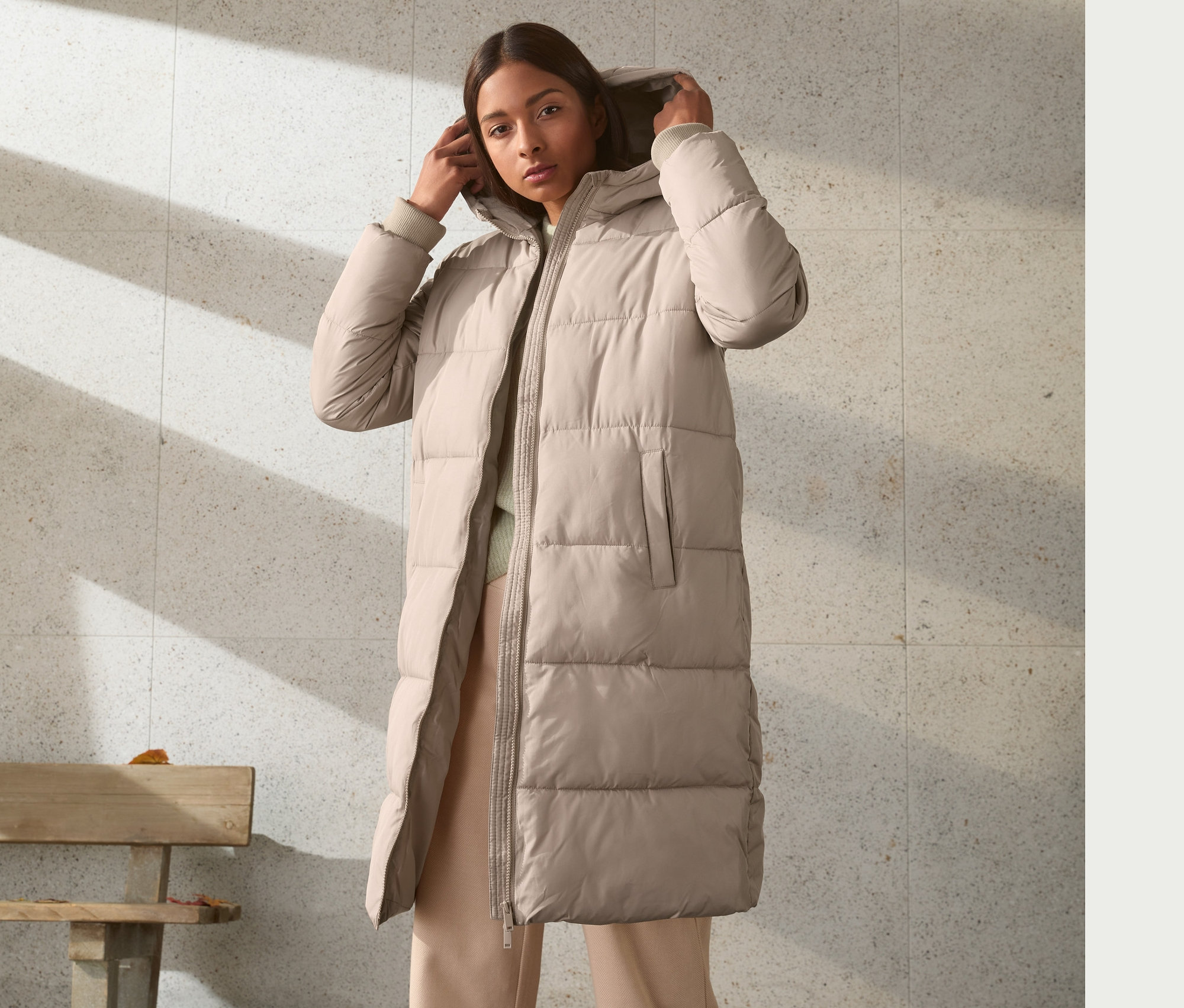 Kobieta poprawia kaptur płaszcza pikowanego.