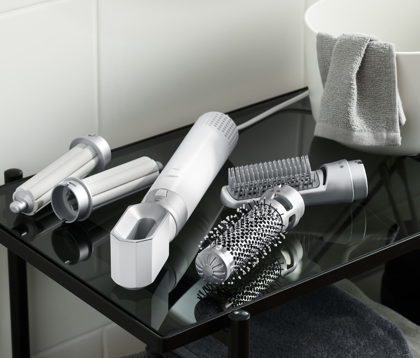 Na szklanej półce w łazience leży suszarko-lokówka 5 w 1 i jej nasadki.