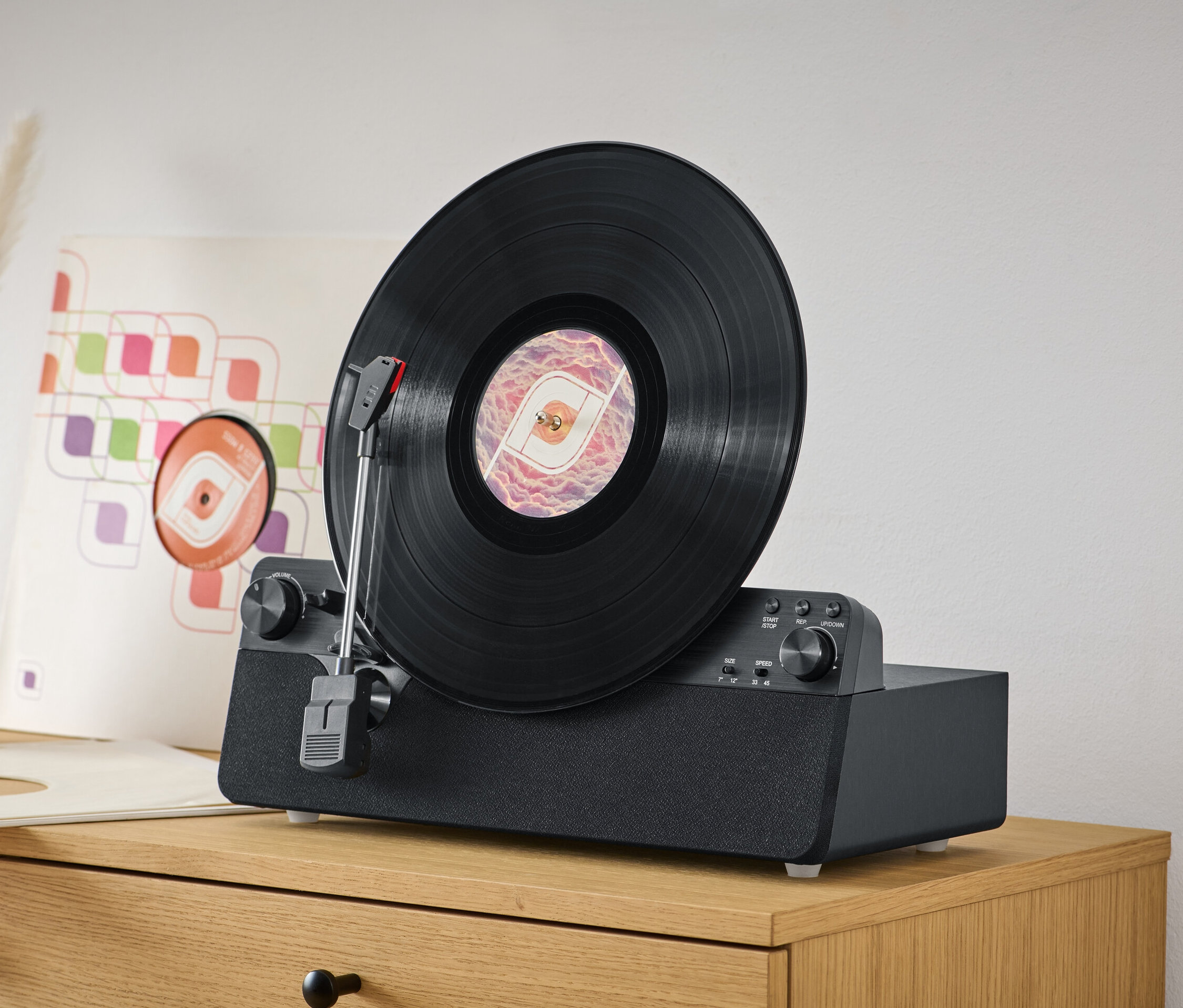 Czarna płyta winylowa odtwarzana jest na pionowym gramofonie z wbudowanymi głośnikami, stojącym na drewnianej komodzie.