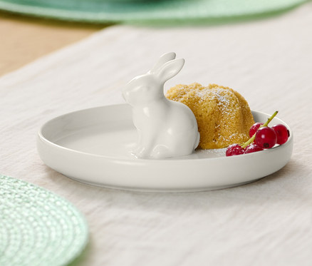 Talerz z zającem wielkanocnym, babka i czerwone porzeczki na stole.