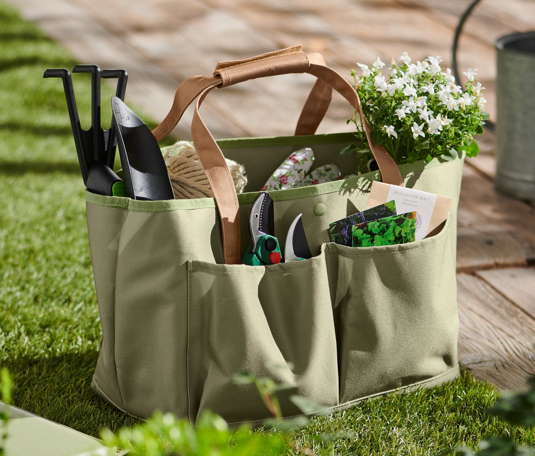 Torba ogrodnicza z narzędziami, kwiatami i nasionami na trawie.