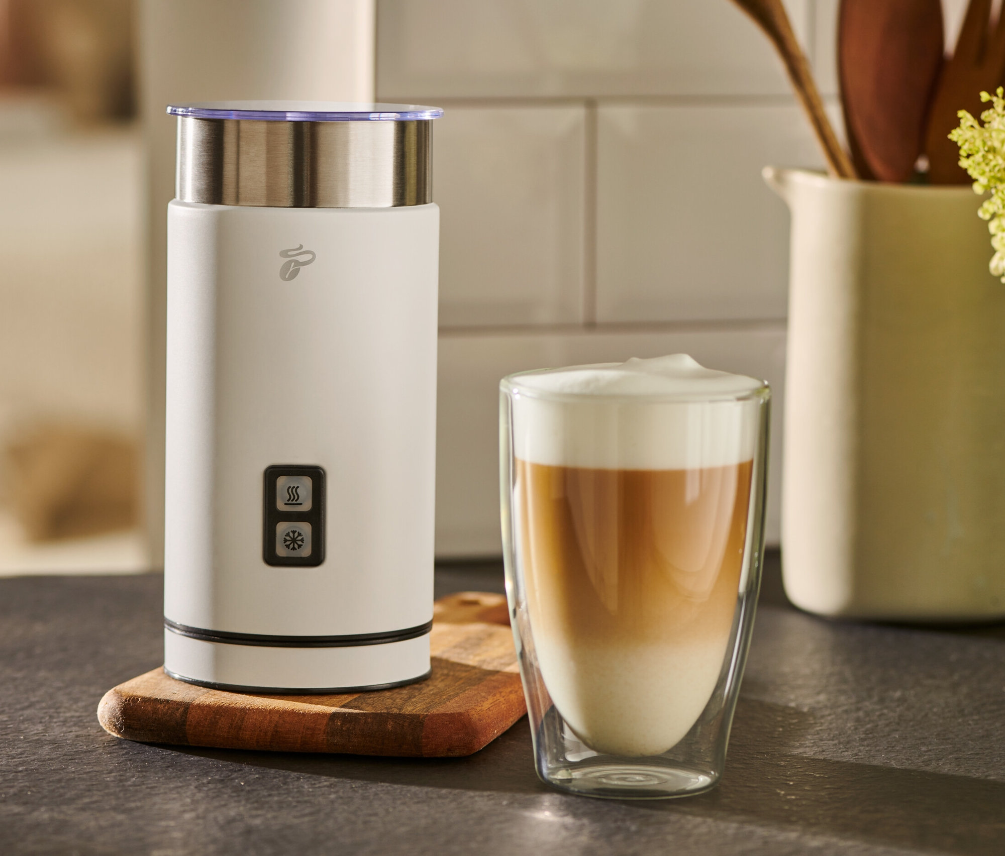 Biały elektryczny spieniacz do mleka stoi obok szklanki kawy z mlekiem.