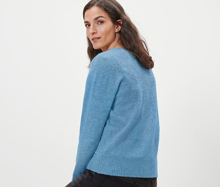 Kobieta siedzi na drewnianym stołku i ma na sobie jasnoniebieski rozpinany sweter z zawartością wełny.