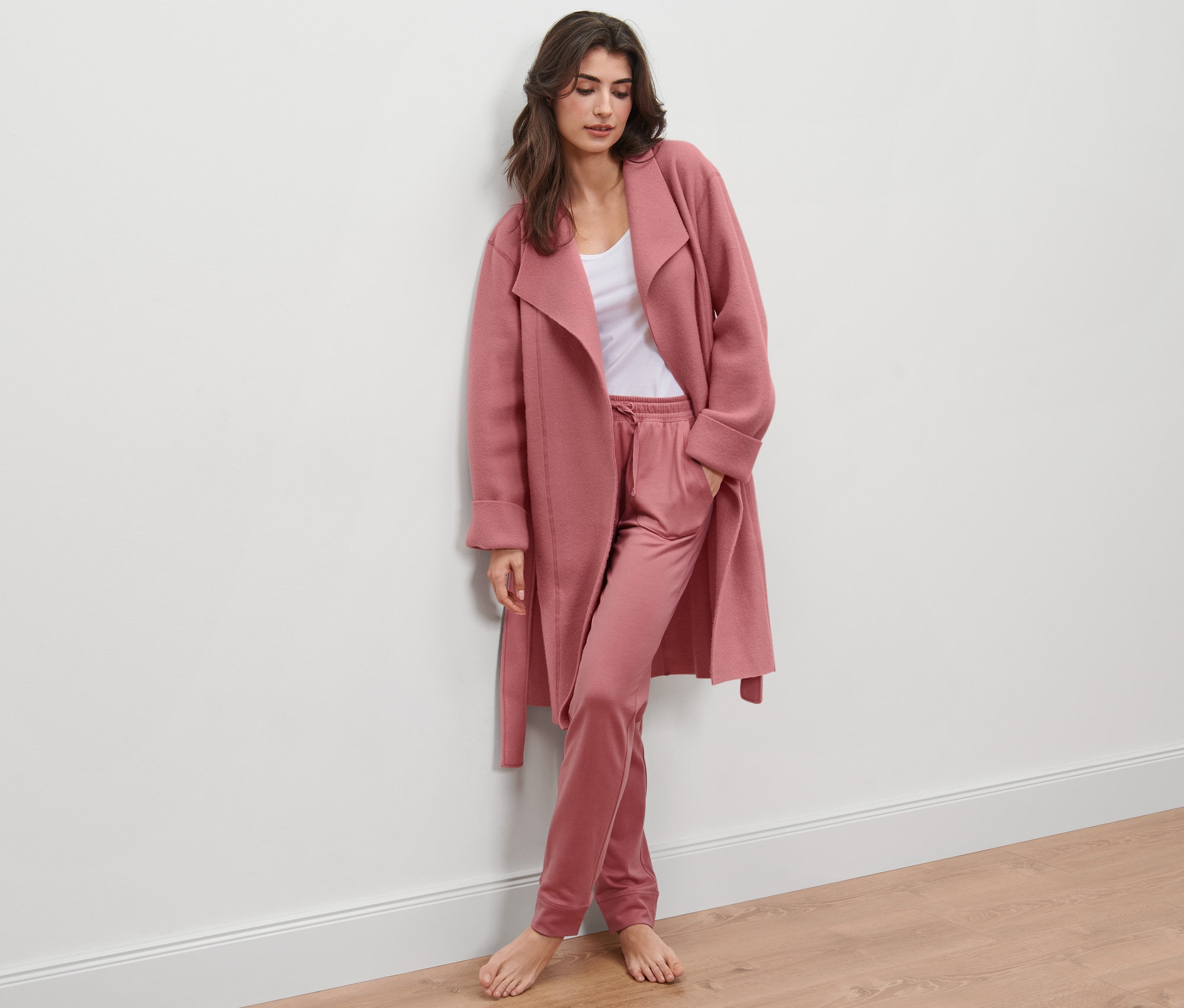 Kobieta oparta o ścianę ma na sobie polarowy płaszcz i spodnie.