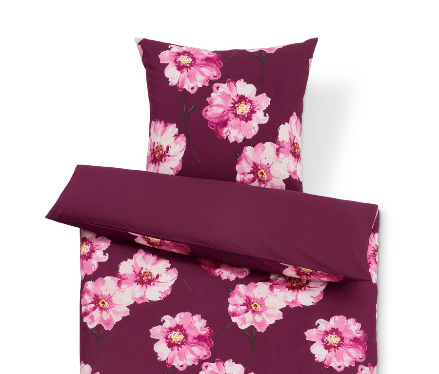 Fioletowa pościel we wzory kwiatowe i jednolita fioletowa poduszka.