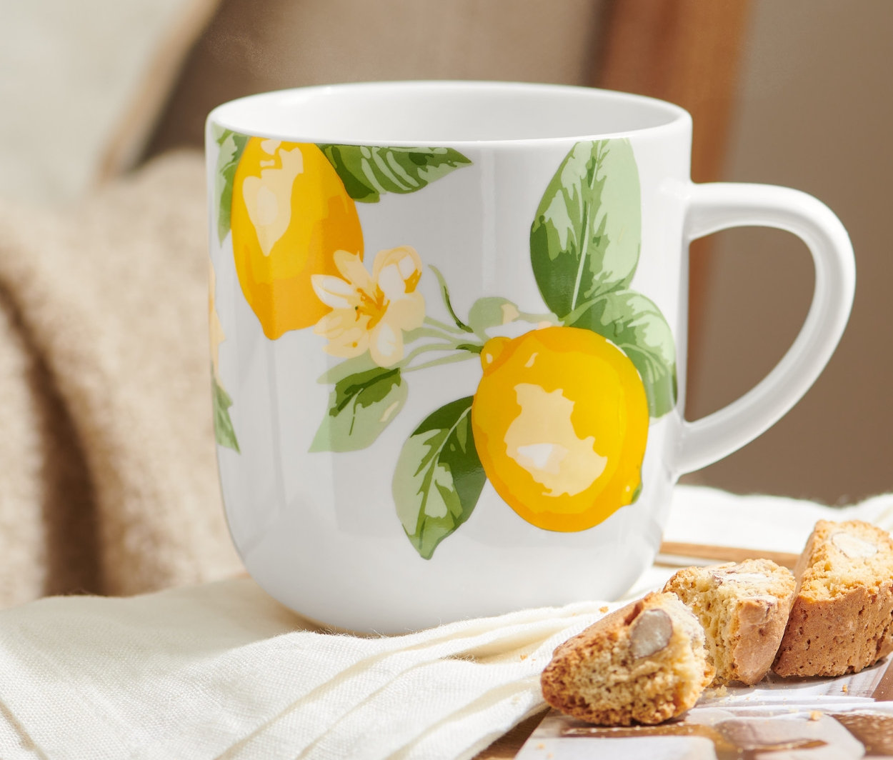 Na drewnianym krześle stoi Duży kubek z motywem cytryn, obok leżą biała serwetka i ciastka.