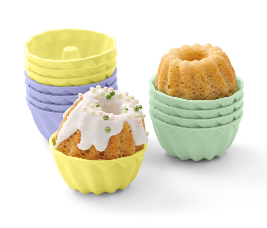 Minibabeczka w żółtej foremce, polana białą polewą i ozdobiona kolorowymi kuleczkami. W tle foremki do minibabeczek, 12 sztuk.