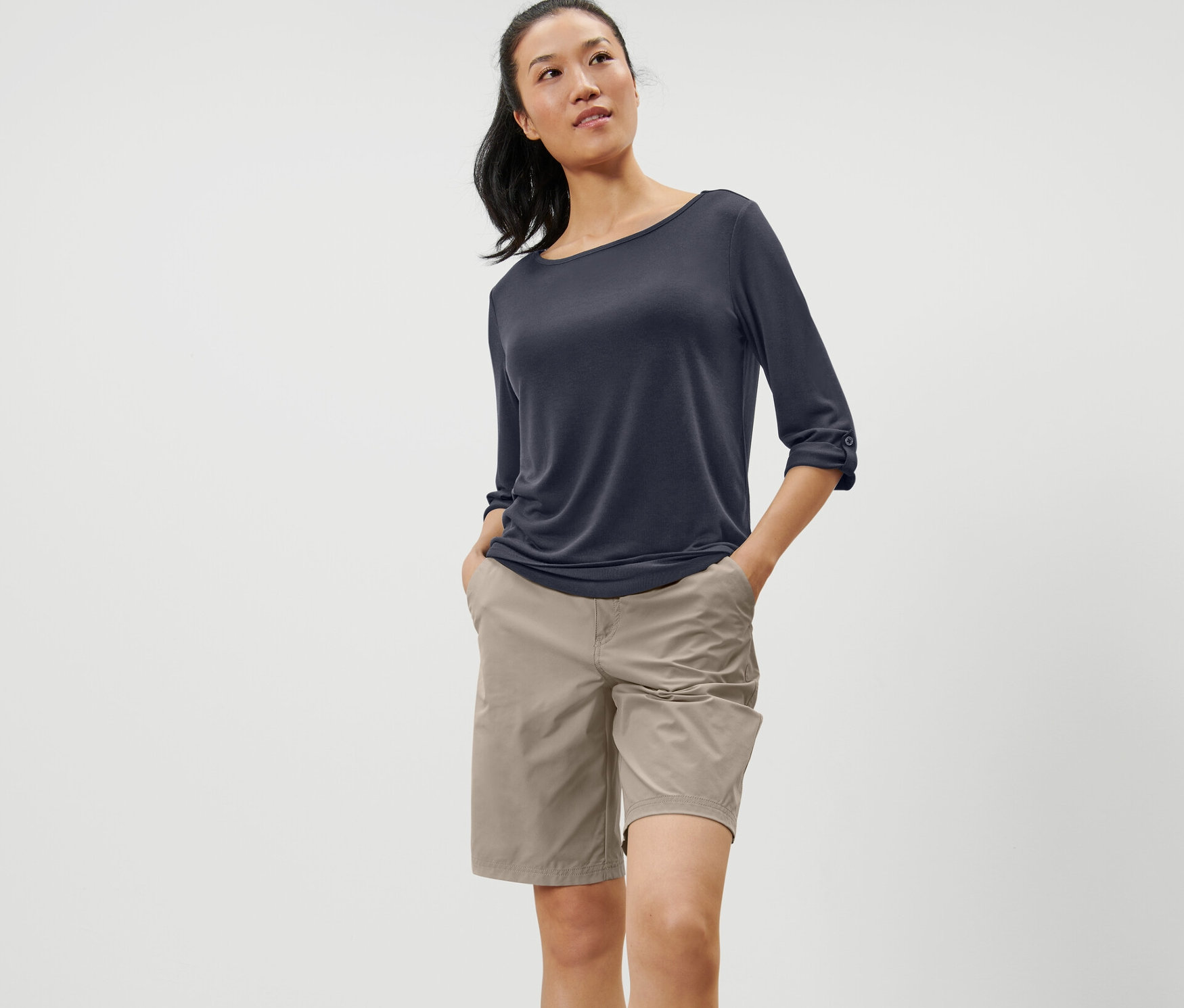 Kobieta stoi z rękami w kieszeniach, ubrana w granatową koszulkę funkcyjną z rękawami o długości 3/4.