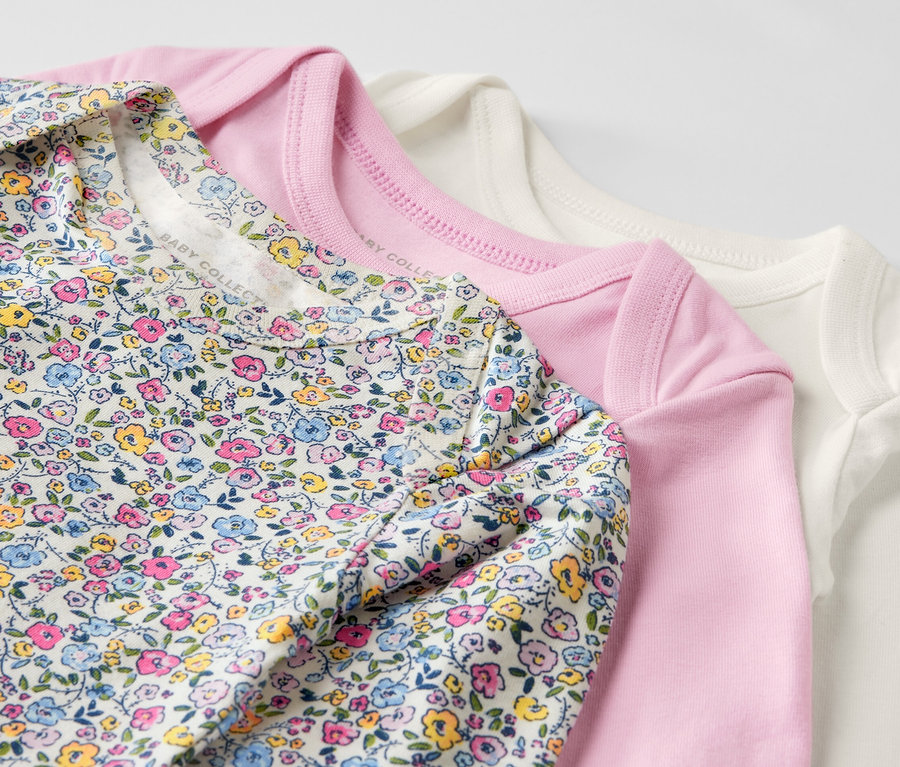 Trzy różowe body niemowlęce rosnące z dzieckiem leżą na sobie.